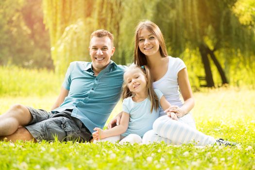 Happy smiling family sitting on the grass in the park and looking at the camera.