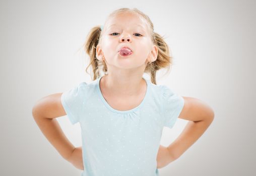 Cute little girl standing with hands on hips and sticking out tongue.