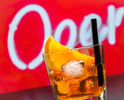 detail of glass of spritz aperitif aperol cocktail with orange slices and ice cubes on bar table, disco atmosphere background, lounge bar concept