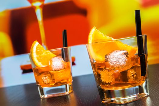 two glasses of spritz aperitif aperol cocktail with orange slices and ice cubes on bar table, disco atmosphere background, lounge bar concept