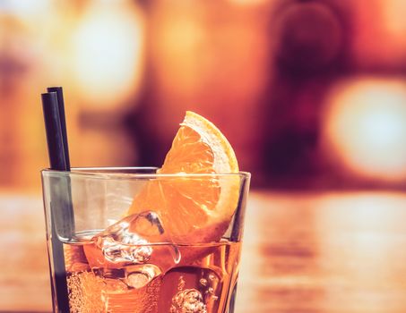 detail of glass of spritz aperitif aperol cocktail with orange slices and ice cubes on bar table, vintage atmosphere background, lounge bar concept