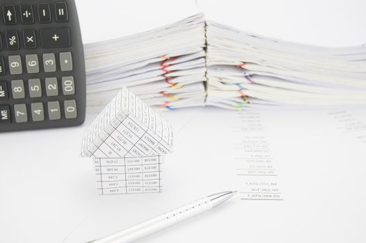 Silver pen and house on balance sheet have calculator place vertical with paper of report and paperwork as background.