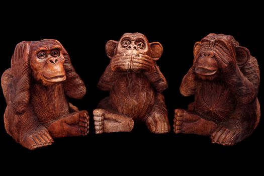 Three wise monkeys. Figurines of wood on a black background.