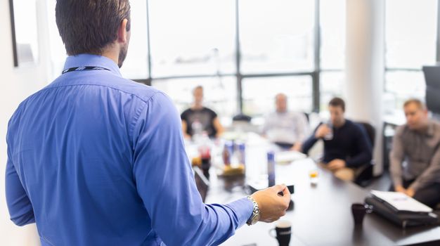 Business man making a presentation at office. Business executive delivering a presentation to his colleagues during meeting or in-house business training, explaining business plans to his employees. 