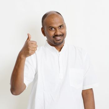 Portrait of happy mature casual business Indian man thumb up, standing on plain background with shadow.