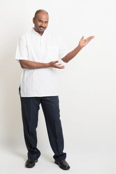 Full length Indian casual man hands showing something on copy space, standing on plain background with shadow.