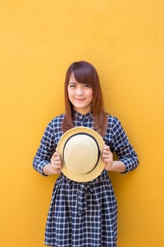 smiling woman wear in dress hand holding hat on yellow cement wall background