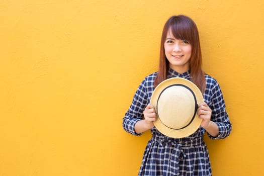 smiling woman wear in dress hand holding hat on yellow cement wall background