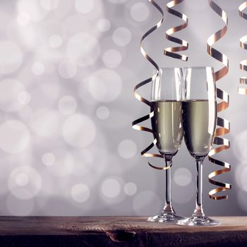 Two glasses of champagne and ribbons on light bokeh background