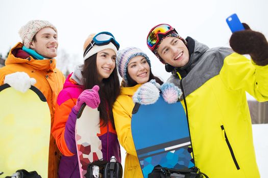 winter sport, leisure, friendship, technology and people concept - happy friends with snowboards and smartphone taking selfie