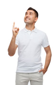 happiness, gesture and people concept - smiling man pointing finger up