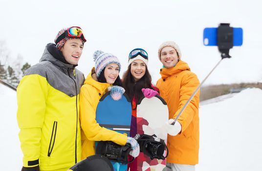 winter sport, leisure, friendship, technology and people concept - happy friends with snowboards and smartphone taking selfie