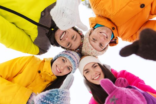 winter, leisure, friendship and people concept - happy friends standing in circle outdoors, showing thumbs up and and looking down