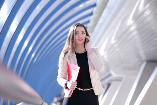 Young Businesswoman with folder talking on the phone in modern building