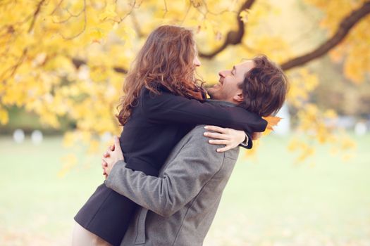 Smiling couple hugging in autumn park on yellow maple tree background