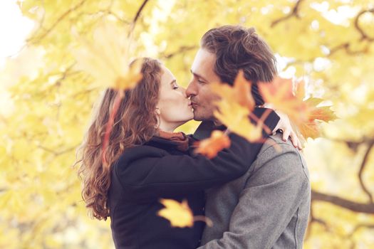 Beautiful couple with maple leaves kissing in autumn park