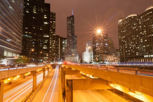 Chicago buildings, towering overhead, overground railway, urban road and lights streams with light flares from street lights, Illinois, USA