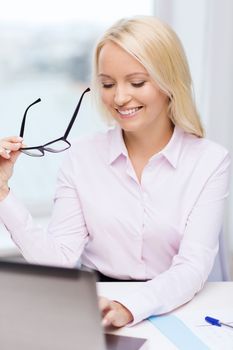 education, business and technology concept - smiling businesswoman or student with eyeglasses and laptop computer in office