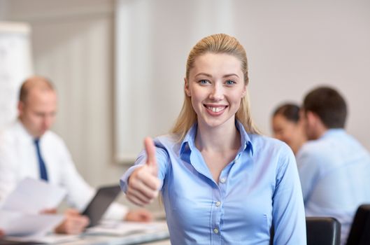 business, people, gesture and teamwork concept - smiling businesswoman showing thumbs up with group of businesspeople meeting in office