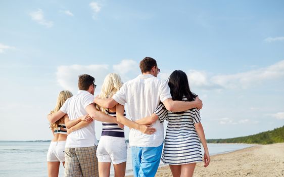 summer, holidays, sea, tourism and people concept - group of smiling friends hugging and walking on beach from back