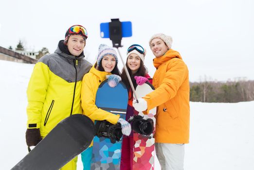 winter sport, leisure, friendship, technology and people concept - happy friends with snowboards and smartphone taking selfie