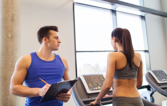 sport, fitness, lifestyle, technology and people concept - woman and trainer with clipboard working out on treadmill in gym