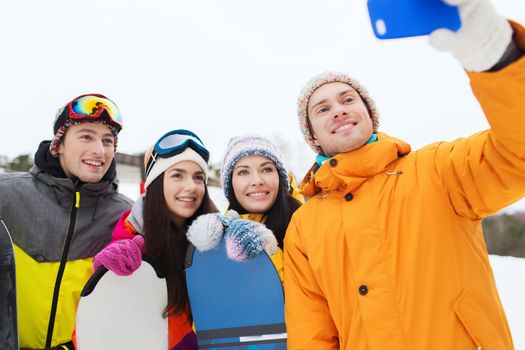 winter sport, leisure, friendship, technology and people concept - happy friends with snowboards and smartphone taking selfie