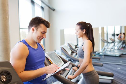 sport, fitness, lifestyle, technology and people concept - happy woman and trainer with clipboard working out on treadmill in gym