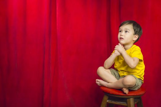 Handsome Mixed Race Boy Sitting on Stool in Front of Red Curtain.