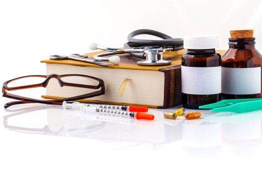 Stethoscope on a textbooks and bottle of pills isolated on white background.