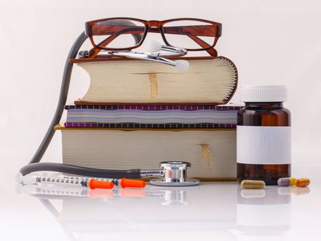 Stethoscope on a textbooks and bottle of pills isolated on white background.