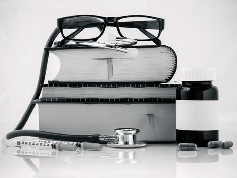 Stethoscope on a textbooks and bottle of pills isolated on white background.