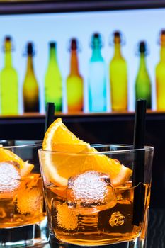 detail of two glasses of spritz aperitif aperol cocktail with orange slices and ice cubes on bar table, disco atmosphere background, lounge bar concept