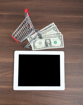 Tablet with money and shopping cart on wooden table