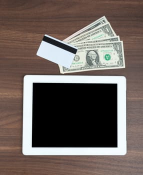 Tablet with money and credit card on wooden table