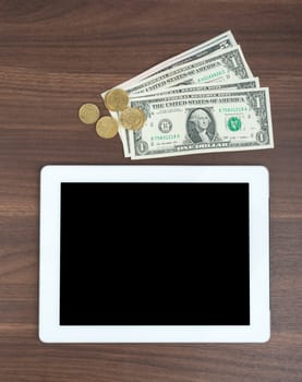 Tablet with money on wooden table, top view