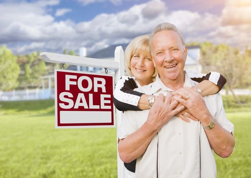 Happy Senior Couple Front of For Sale Real Estate Sign and House.