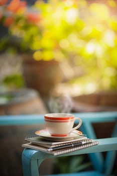 Coffee cup, notebooks, and pen on blue veran armchair in afternoon time