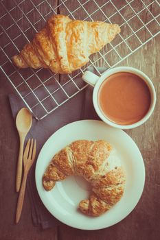 Butter croissant and whole wheat croissant with a cup of hot chocolate on wood table in morning time with film filter effect