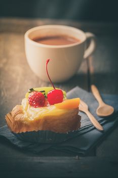 Fruit danish pastry with hot chocolate on wood table in morning time with film filter effect