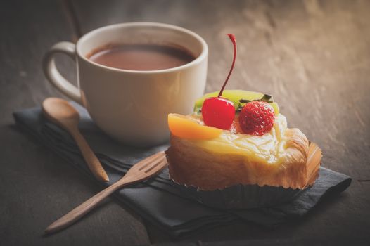 Fruit danish pastry with hot chocolate on wood table in morning time with film filter effect