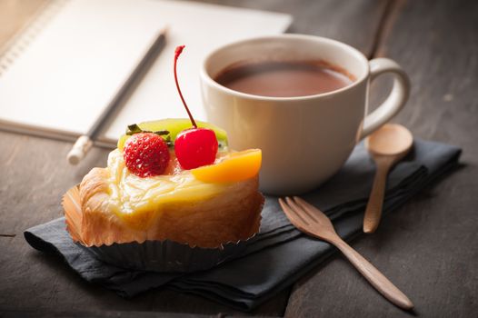 Fruit danish pastry with hot chocolate and opened notebook on wood table in morning time