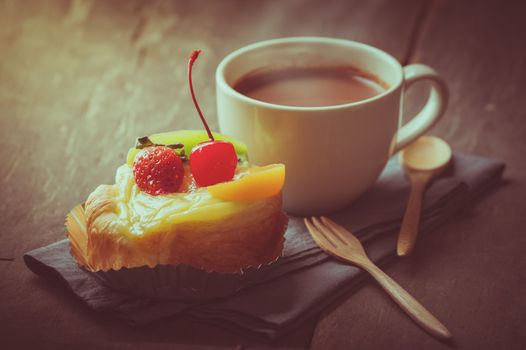 Fruit danish pastry with hot chocolate on wood table in morning time with film filter effect