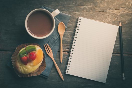 Fruit danish pastry with hot chocolate and opened notebook with blank area for text or message on wood table in morning time with film filter effect