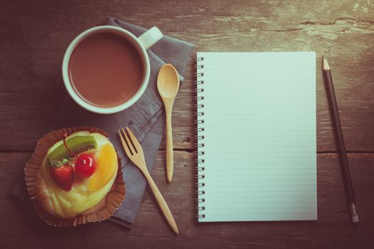 Fruit danish pastry with hot chocolate and opened notebook with blank area for text or message on wood table in morning time with film filter effect