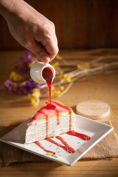 Rainbow crepe cake with male left hand pouring strawberry sauce on top in afternoon time with low key scene