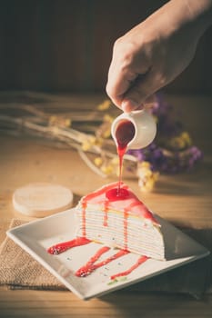 Rainbow crepe cake with male right hand pouring strawberry sauce on top in afternoon time with film filter effect