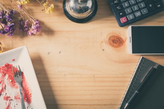 Wood table background with blank area for text or message, dirty dessert plate, flowers, calculator and smartphone as frame around in afternoon time with film filter effect