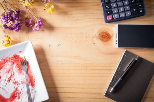 Wood table background with blank area for text or message, dirty dessert plate, flowers, calculator and smartphone as frame around in afternoon time