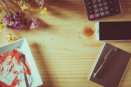 Wood table background with blank area for text or message, dirty dessert plate, flowers, calculator and smartphone as frame around in afternoon time with film filter effect
